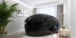 A black Dreampod Vmax Float Pod in a minimalist, well-lit room with greenery