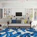 A bright living room showcases the Couristan Covington Indoor/Outdoor Rug - Palm Leaves/Blue under a white sofa with striped and solid pillows