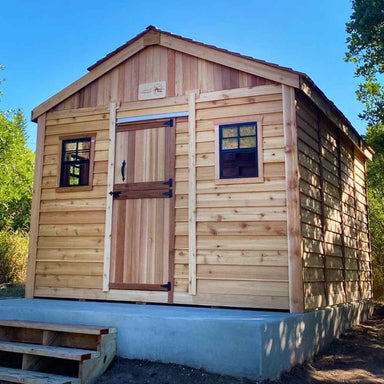 A charming Outdoor Living Today 12×16 Sunshed Garden Shed with a gabled roof, rustic cedar panels, and two small front windows