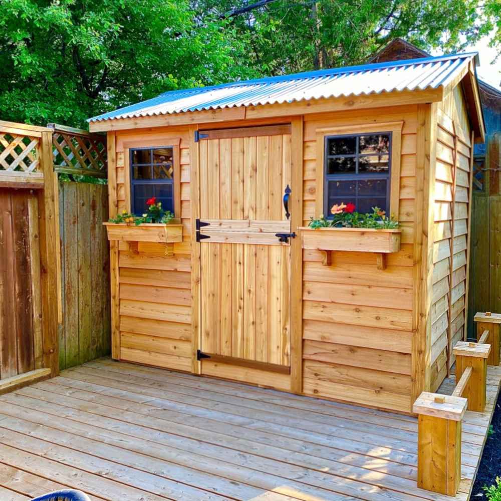 A charming wooden shed with flower boxes and a corrugated metal roof stands on a deck, showcasing the Outdoor Living Today 9×6 Cabana Garden Shed
