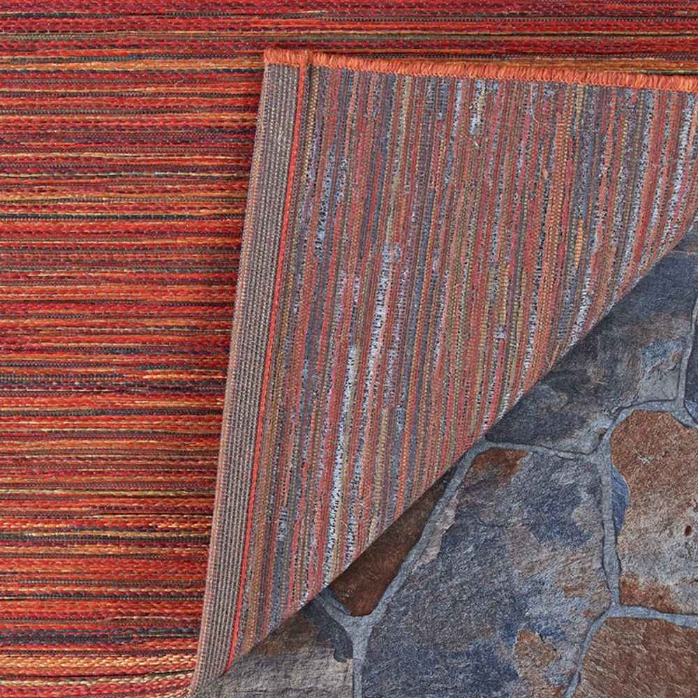 A close-up of the Couristan Cape Indoor/Outdoor Rug - Hinsdale/Crimson-Multi shows its textured weave and the underside corner flipped to reveal the backing on a stone floor