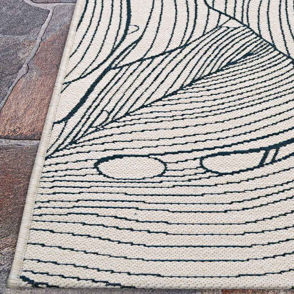 A close-up of the Couristan Castille Indoor/Outdoor Rug - Palma/Petrol shows detailed stitching of the leaf pattern along the edge