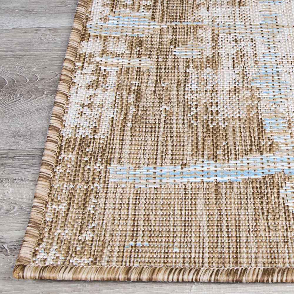 A close-up of the Couristan Charm Indoor/Outdoor Rug - Tiverton/Sand-Ivory corner reveals tightly bound edges and blended tones of sand, ivory, and sky blue