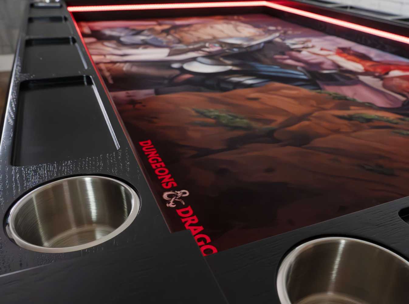 A close-up of the Game Theory Tables Origins Lit Dungeons & Dragons table corner, highlighting the polished metal cup holders and intricate game artwork