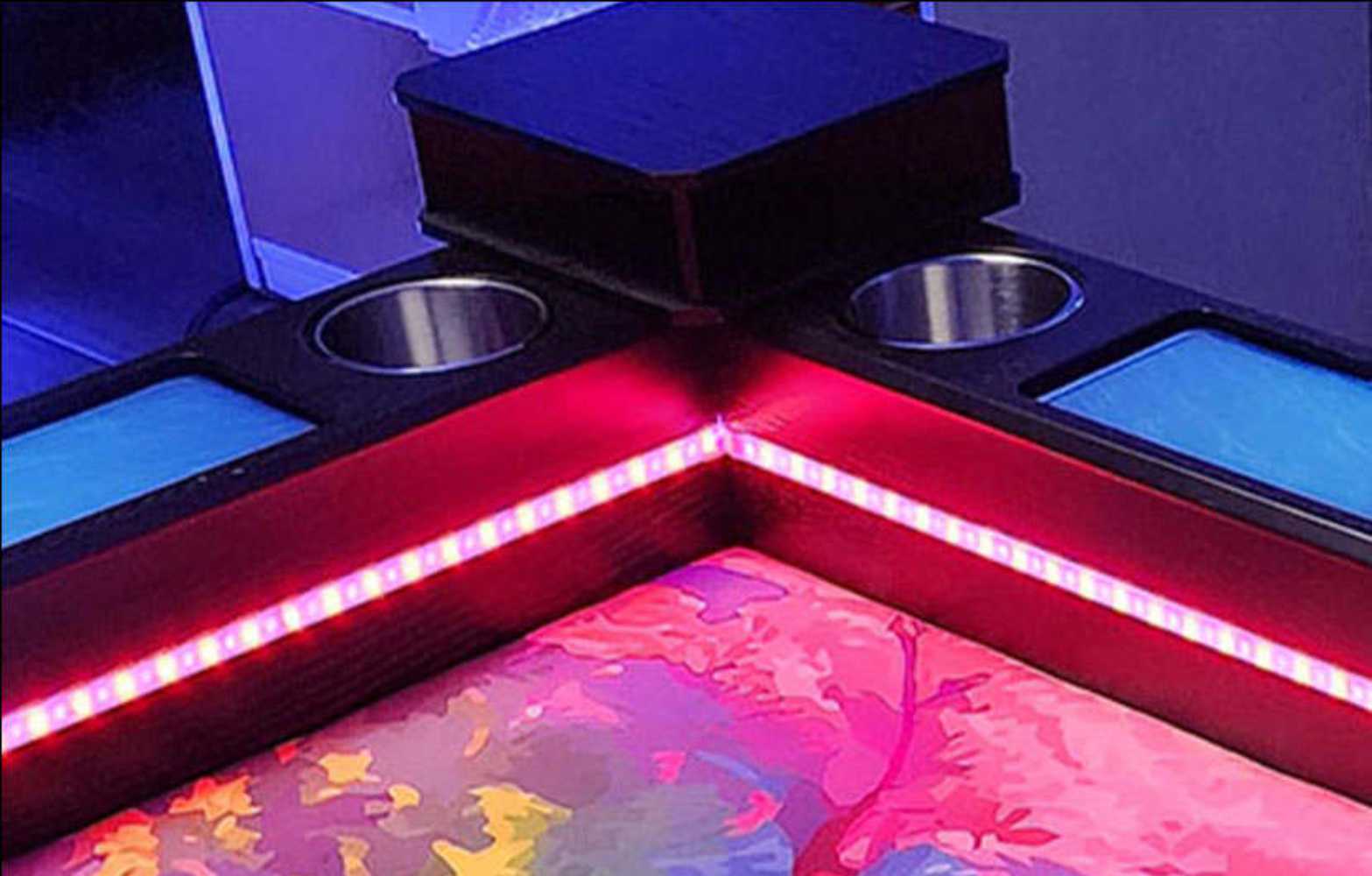 A close-up of the Game Theory Tables Origins Lit table's illuminated corner, featuring red LED lighting and built-in cup holders