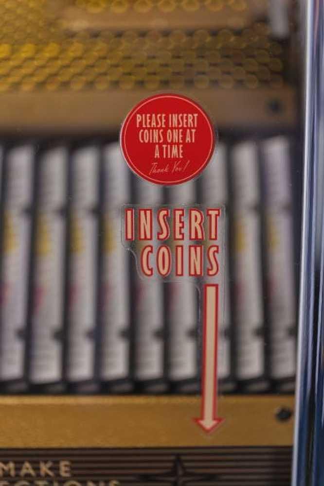 A close-up of the coin slot on the Crosley Rocket 80 CD Bluetooth Full-Size Jukebox - Oak shows bold instructions inviting users to insert coins