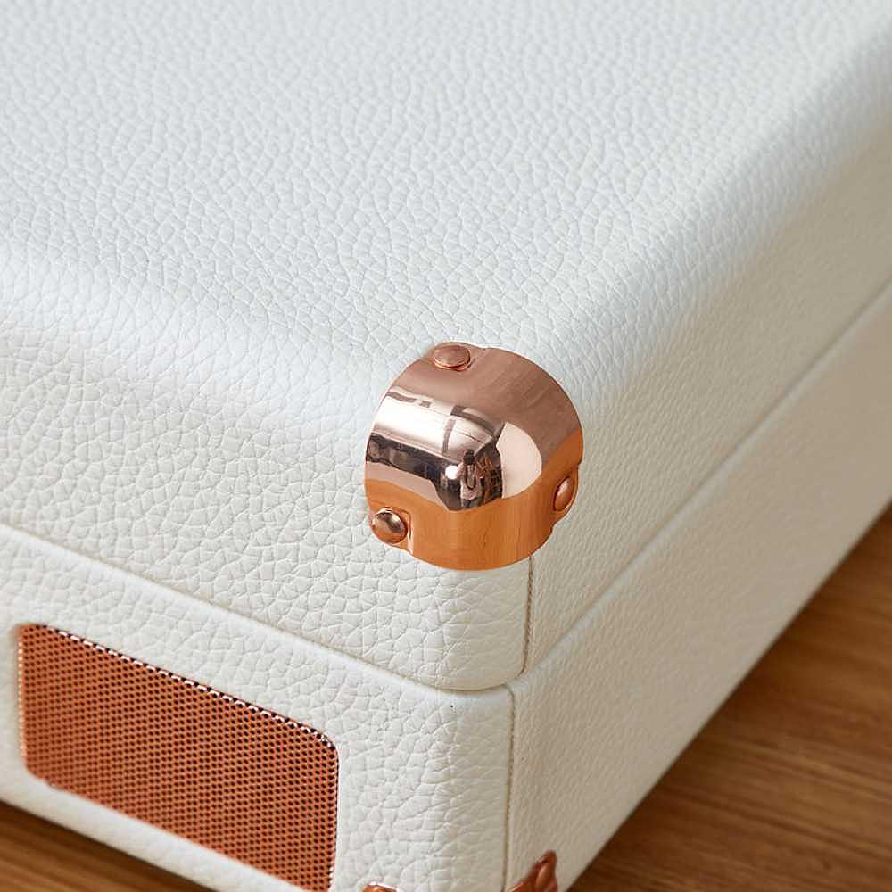 A close-up of the corner of Arkrocket Curiosity Suitcase Bluetooth Turntable (Cream Rose Gold) with cream leather texture and rose gold protective corner caps