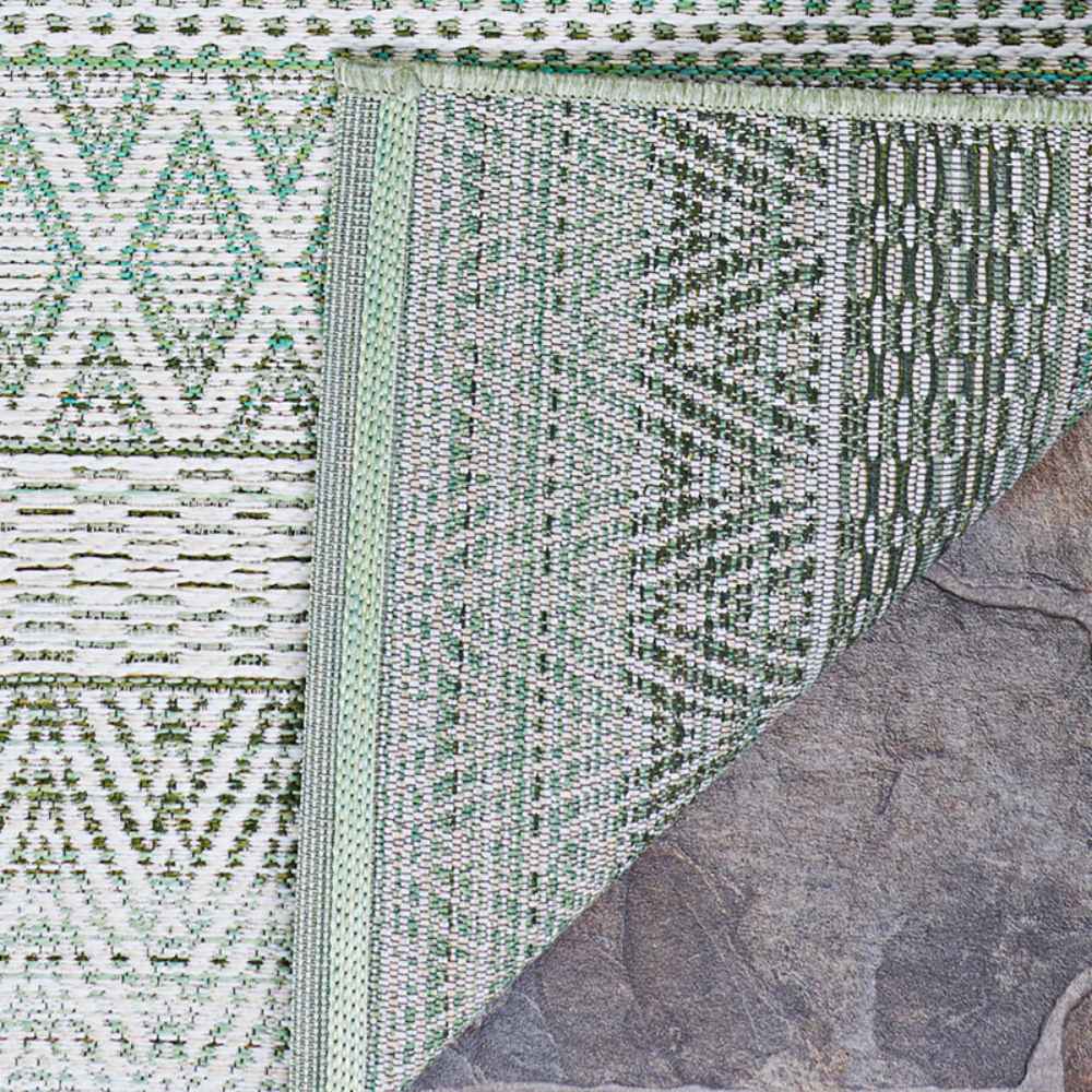 A close-up of the corner of the Couristan Cape Indoor/Outdoor Rug - Gables/Palm shows its intricate green and ivory woven patterns against a stone floor
