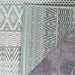 A close-up of the corner of the Couristan Cape Indoor/Outdoor Rug - Gables/Palm shows its intricate green and ivory woven patterns against a stone floor