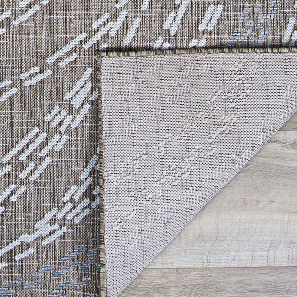 A close-up of the corner of the Couristan Charm Indoor/Outdoor Rug - Aurora/Twig shows its durable woven texture and non-slip backing flipped over on a wooden floor