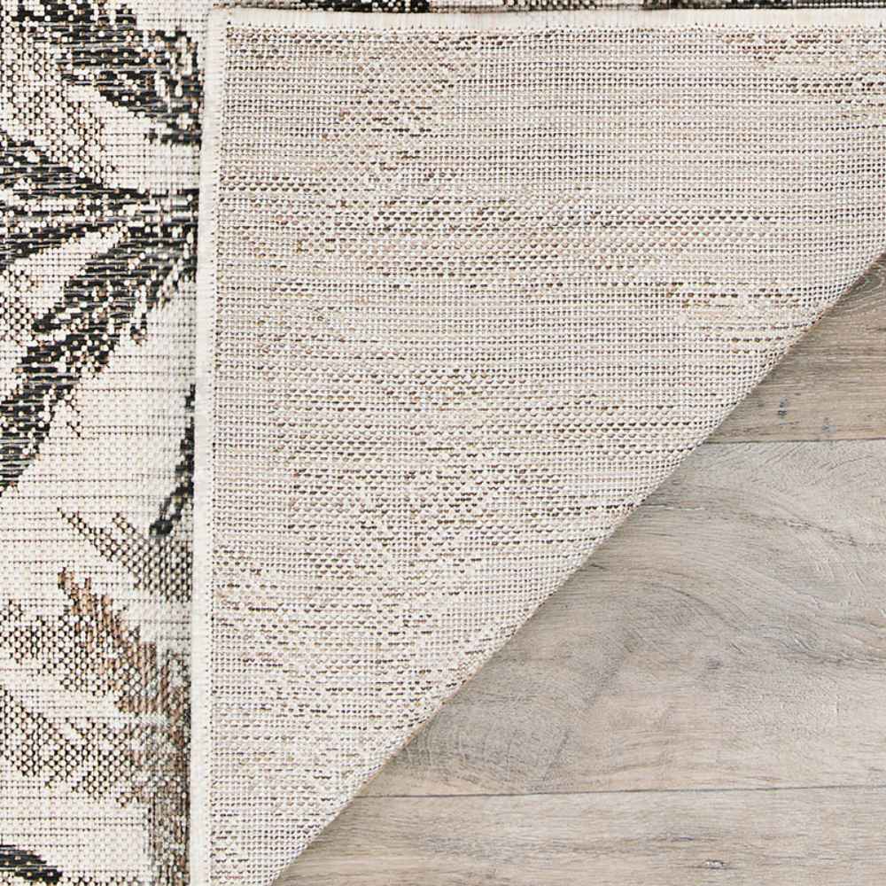 A close-up of the corner of the Couristan Charm Indoor/Outdoor Rug - Kimberly/Naturals is lifted to show its textured, durable underside on wood flooring