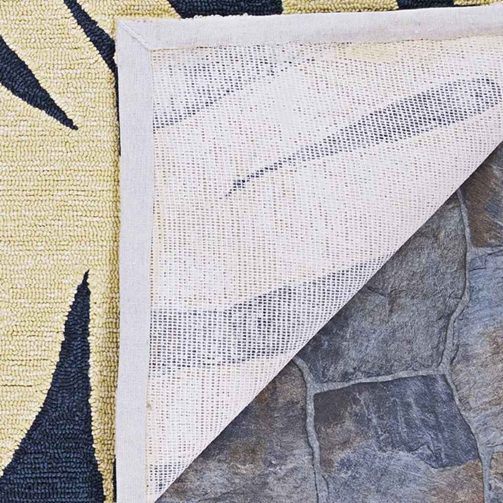 A close-up of the corner of the Couristan Covington Indoor/Outdoor Rug - Palms/Navy shows the woven underside revealing the stone patio beneath