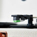 A close-up of the needle and cartridge of the Arkrocket Curiosity Suitcase Bluetooth Turntable (Cream Rose Gold), with a focus on the green tip and black arm