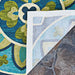 A close-up shows the back corner of the Couristan Covington Indoor/Outdoor Rug - Rip Tide/Ocean-Green lifted to reveal its mesh backing on a stone surface