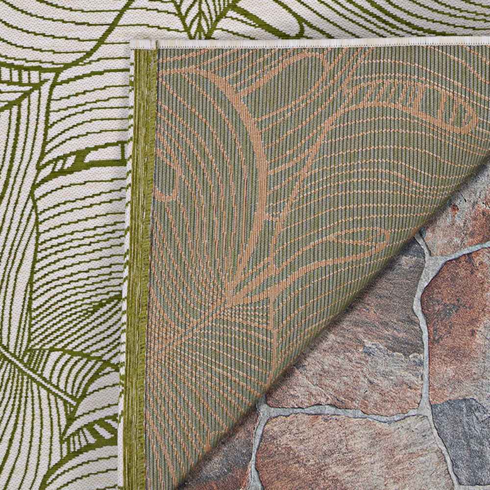A close-up shows the corner of the Couristan Castille Indoor/Outdoor Rug - Palma/Fern folded over, revealing a green and beige leaf pattern with a textured backing