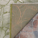 A close-up shows the corner of the Couristan Castille Indoor/Outdoor Rug - Palma/Fern folded over, revealing a green and beige leaf pattern with a textured backing