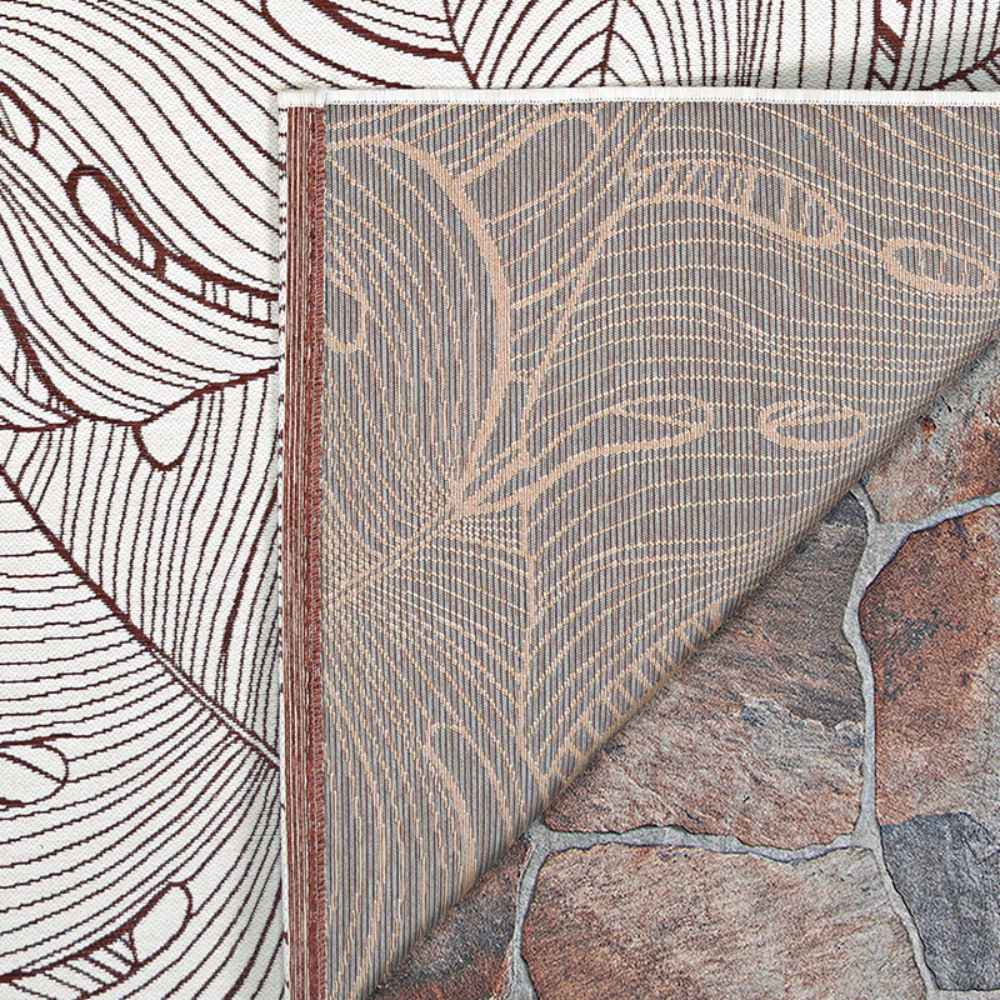 A close-up shows the corner of the Couristan Castille Indoor/Outdoor Rug - Palma/Rouge flipped to reveal its backing and placement on a stone surface
