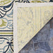 A close-up shows the non-slip backing of the Couristan Covington Indoor/Outdoor Rug - Pegasus/Ivory-Navy-Lime, flipped up on a stone patio