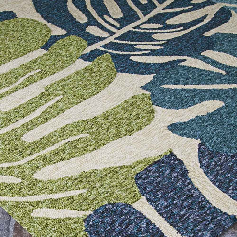 A close-up view shows the textured surface and bold leaf patterns on the Couristan Covington Indoor/Outdoor Rug - Monstera/Cream-Multi