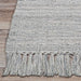 A corner of the Couristan Ascot Indoor/Outdoor Rug - Windowpane/Grey reveals its thick weave and evenly spaced tassels on light wooden flooring