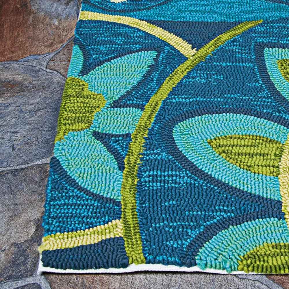 A corner of the Couristan Covington Indoor/Outdoor Rug - Rip Tide/Ocean-Green lies flat against stone pavers