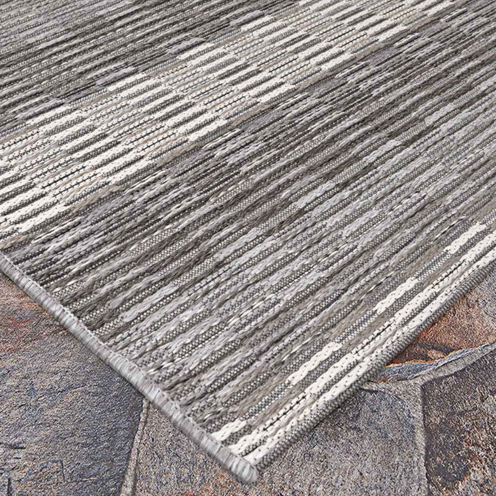 A corner view of the Couristan Cape Indoor/Outdoor Rug - Torrent/Sky Blue-Grey lies flat over a stone surface