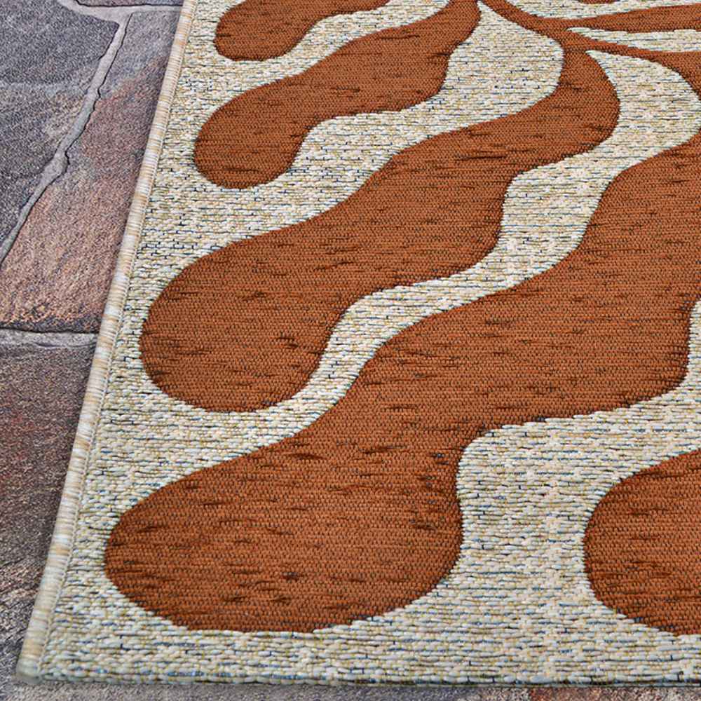 A corner view of the Couristan Castille Indoor/Outdoor Rug - Fiore/Terra-Cotta reveals its intricate curved pattern and tightly bound edges on a stone surface