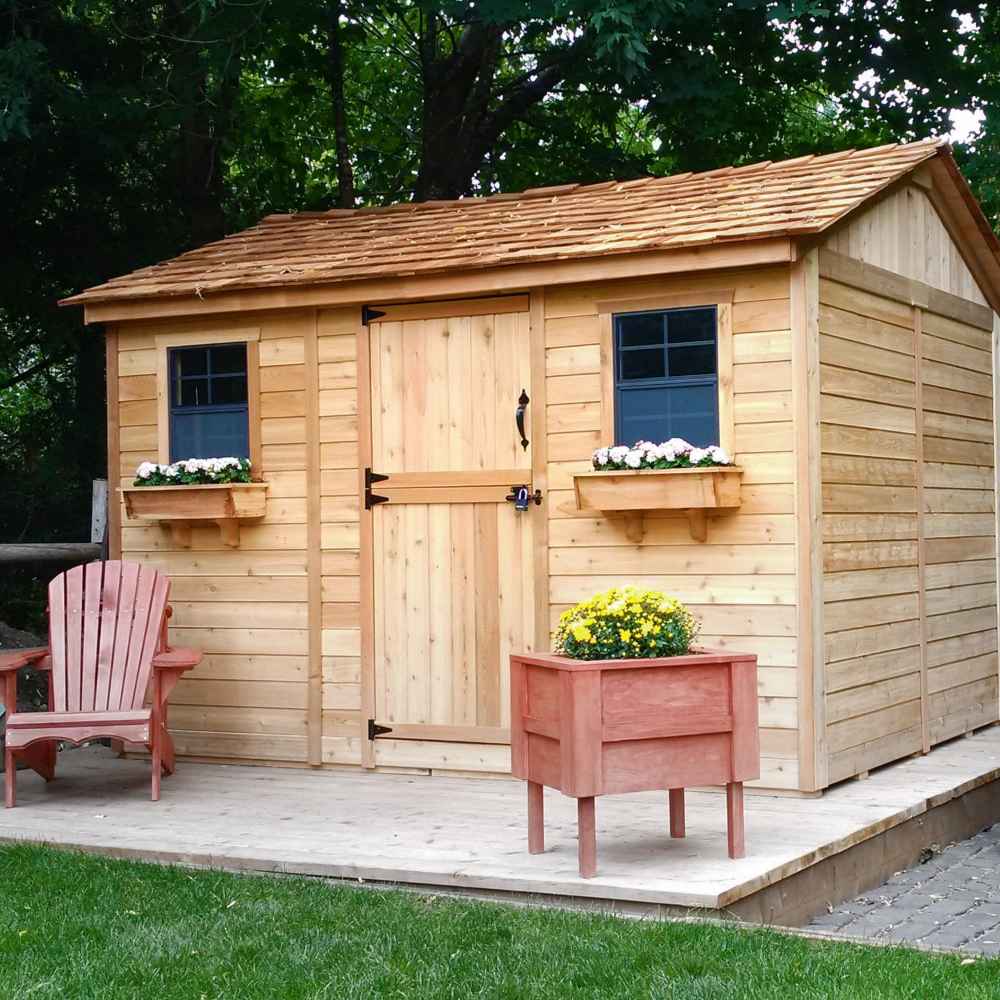 A cozy Outdoor Living Today Large 12×8 Cabana Garden Shed features a central wooden single door, cedar roof, flower boxes under each window, and a rustic porch with Adirondack chairs