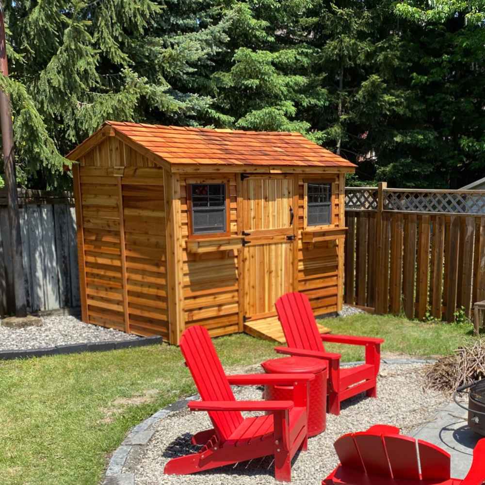 A cozy backyard scene with red chairs faces a cedar shed with double doors, displaying the Outdoor Living Today 9×6 Cabana Garden Shed
