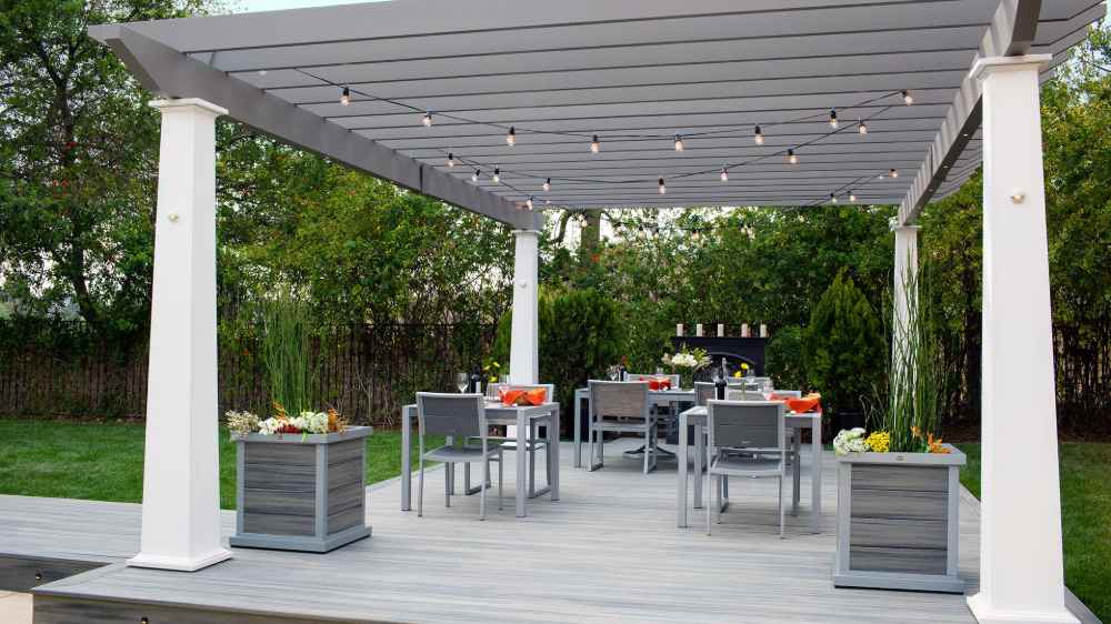 A cozy outdoor dining area features string lights draped across a gray Structureworks Trex Pergola with white posts