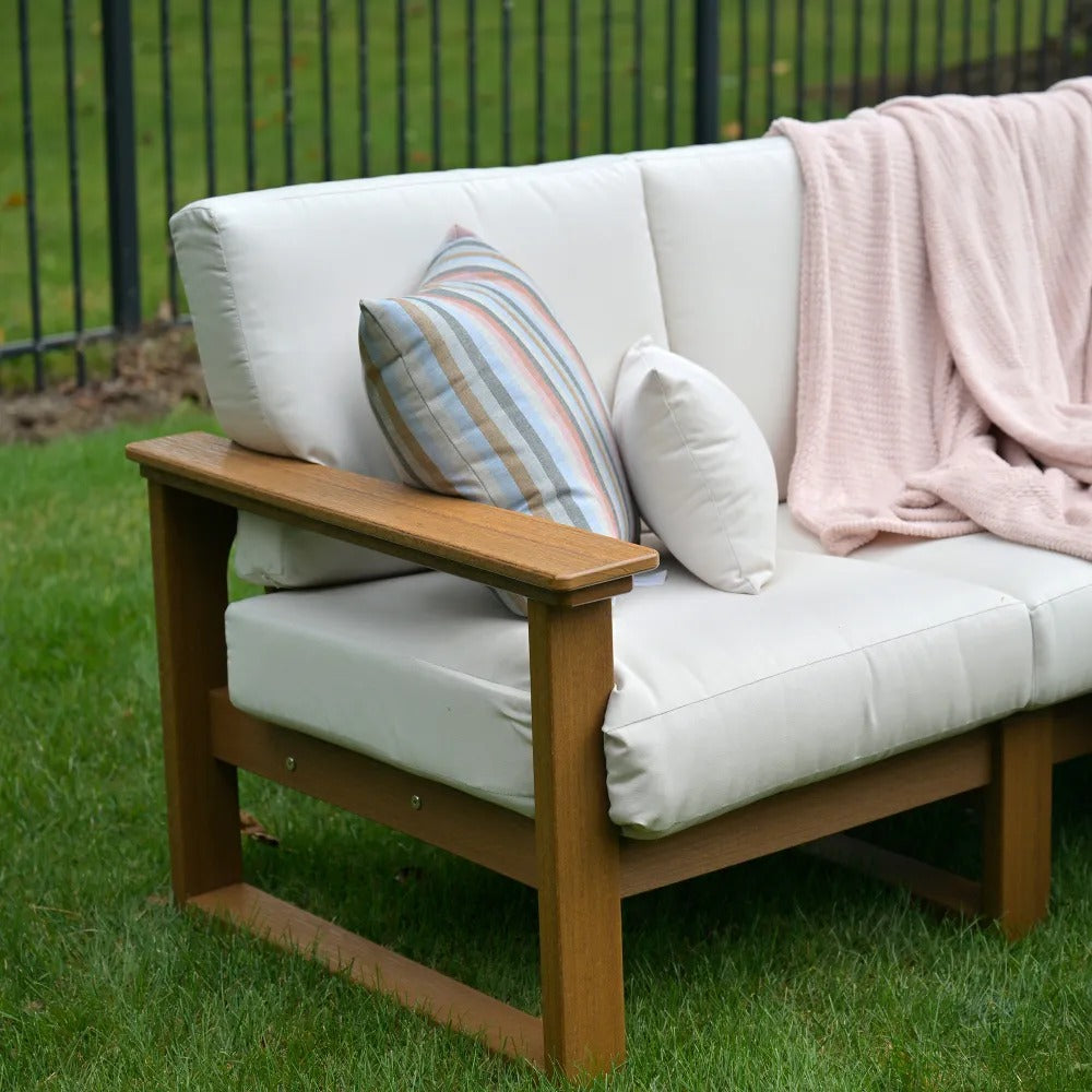 A cozy outdoor poly lumber sofa with white cushions and a brown Luxcraft Armrest.