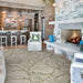 A cozy rustic living room features a stone fireplace and a large leafy-patterned Couristan Castille Indoor/Outdoor Rug - Palma/Petrol covering the wooden floor