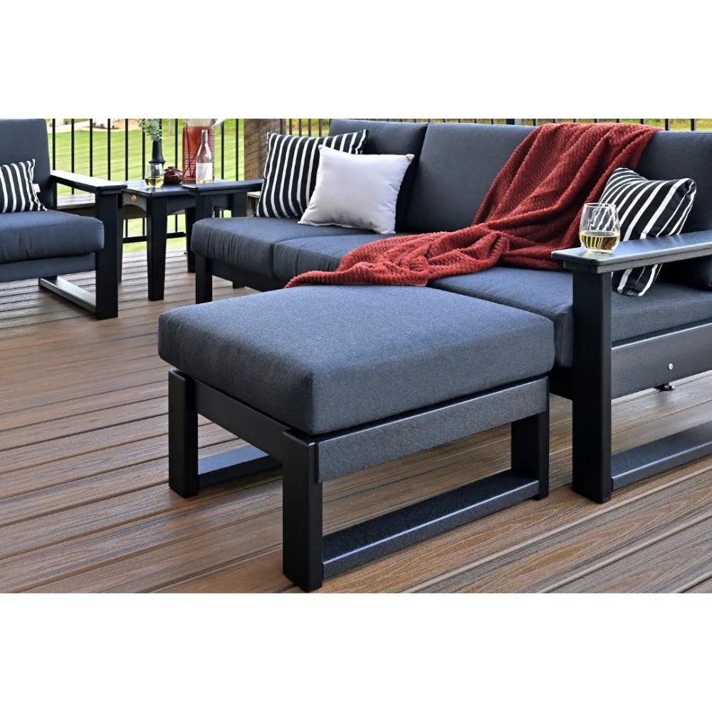 A dark gray LuxCraft Ottoman with a matching cushioned top, placed in front of an outdoor sofa.