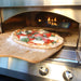 A delicious homemade pizza with fresh basil, mozzarella, and tomatoes is being pulled from the Alfresco Grills 30 Pizza Oven Plus - Built-In