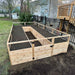 A freshly prepared Outdoor Living Today 8×16 Raised Garden Bed with dark soil stands in a yard near a black metal fence and wooden deck