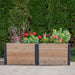 A front-facing view of the Outdoor Living Today 6×3 Urban Raised Garden Bed displays bright blooming flowers set against a hedge