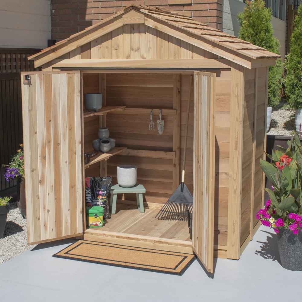 A fully open Outdoor Living Today SpaceMaster 6×4 with Double Door is stocked with gardening tools, pots, and bags inside, set beside blooming flowers outdoors