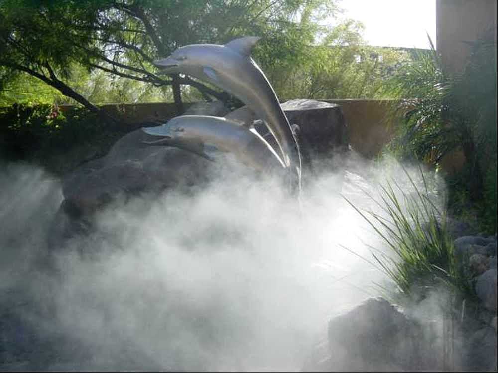 A garden with dolphin statues is filled with fog-like mist produced by the Aeromist Pinnacle 1000 PSI Misting System
