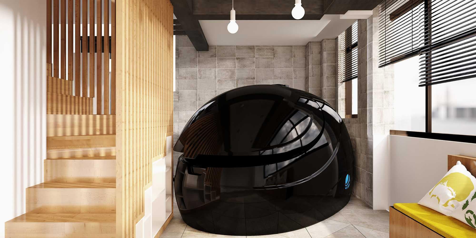 A glossy black Dreampod Sport Float Pod is tucked beside wooden stairs in a cozy, modern room with natural lighting