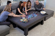 A group of friends intensely strategizing over a board game on the Game Theory Tables The Origins Coffee Table