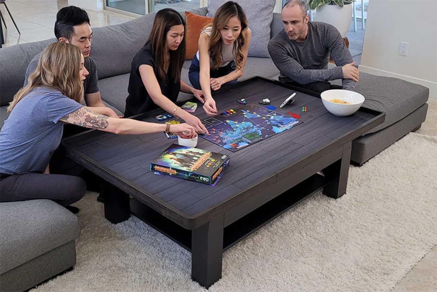 A group of friends intensely strategizing over a board game on the Game Theory Tables The Origins Coffee Table