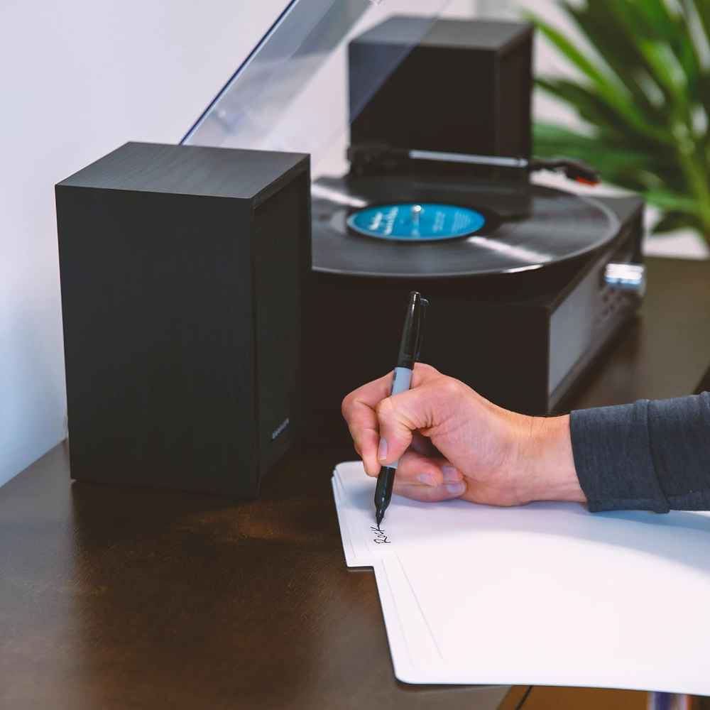 A hand uses a black marker to label a divider near a turntable, emphasizing the usability of Crosley Vinyl Record Dividers - White