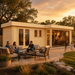 Rectangular light wood cabin with glass doors and a patio where people sit on gray cushioned chairs at sunset.
