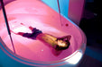 A man floating peacefully in the Dreampod Vmax Float Pod, bathed in soothing pink light, with his hands behind his head in a calm, serene posture