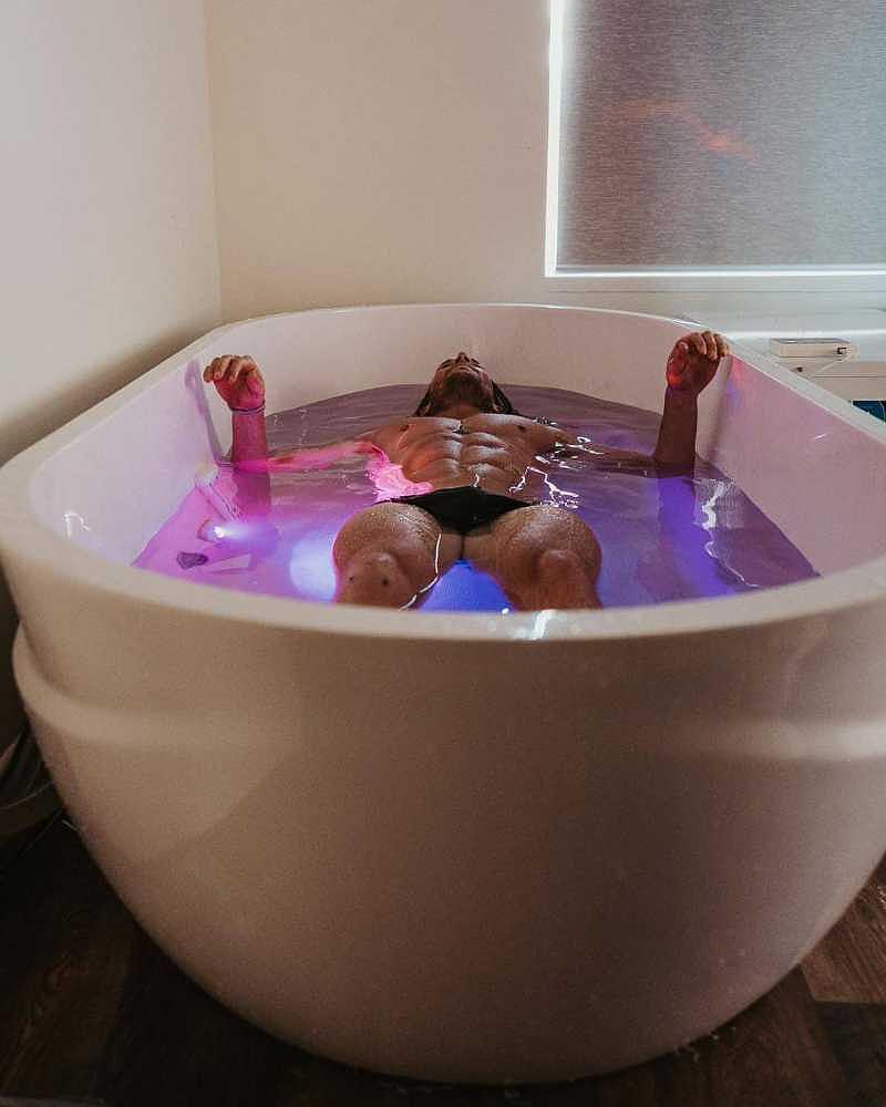 A man lies back in a Dreampod Ice Bath with Chiller indoors, surrounded by calming purple lighting