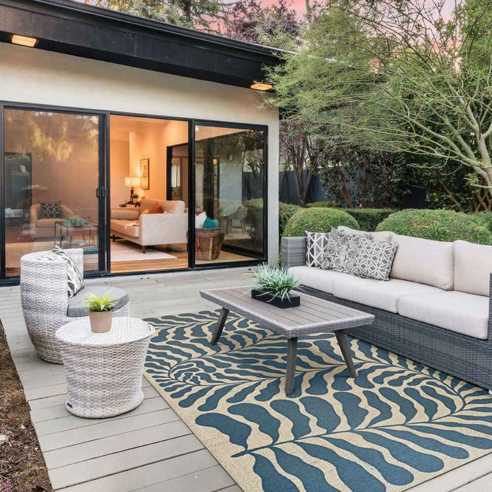 A modern outdoor patio with gray furniture is centered around the Couristan Castille Indoor/Outdoor Rug - Fiore/Petrol