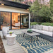 A modern outdoor patio with gray furniture is centered around the Couristan Castille Indoor/Outdoor Rug - Fiore/Petrol