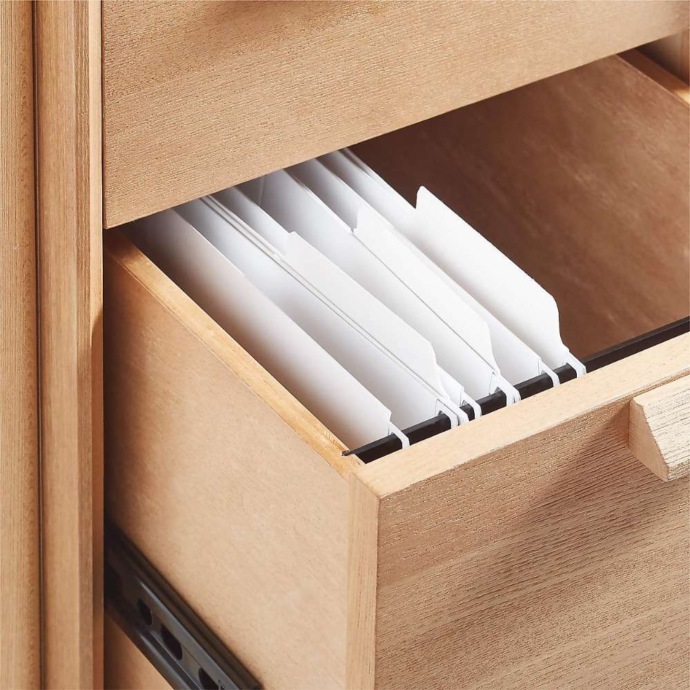 An open file drawer on Crate & Barrel Elias 66" Natural Elm Wood Desk with File Cabinet displays hanging file folders for organized document storage.