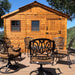 An Outdoor Living Today 12×12 Sunshed Garden Shed stands behind a set of elegant patio chairs on a deck