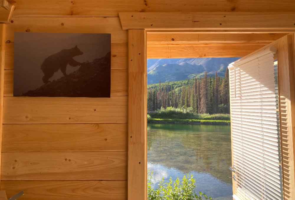 An open doorway reveals a view of a sparkling lake and forest, seen from within the Sawmill Structures The Jumbo Grand Loft 130 SD Garden Room